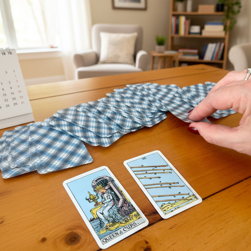 Hand arranging tarot cards on a wooden table with a checkered cloth and a cozy room background.